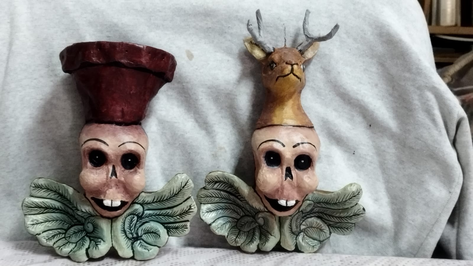 Dos figuras artesanales con rostros de calavera y motivos vegetales