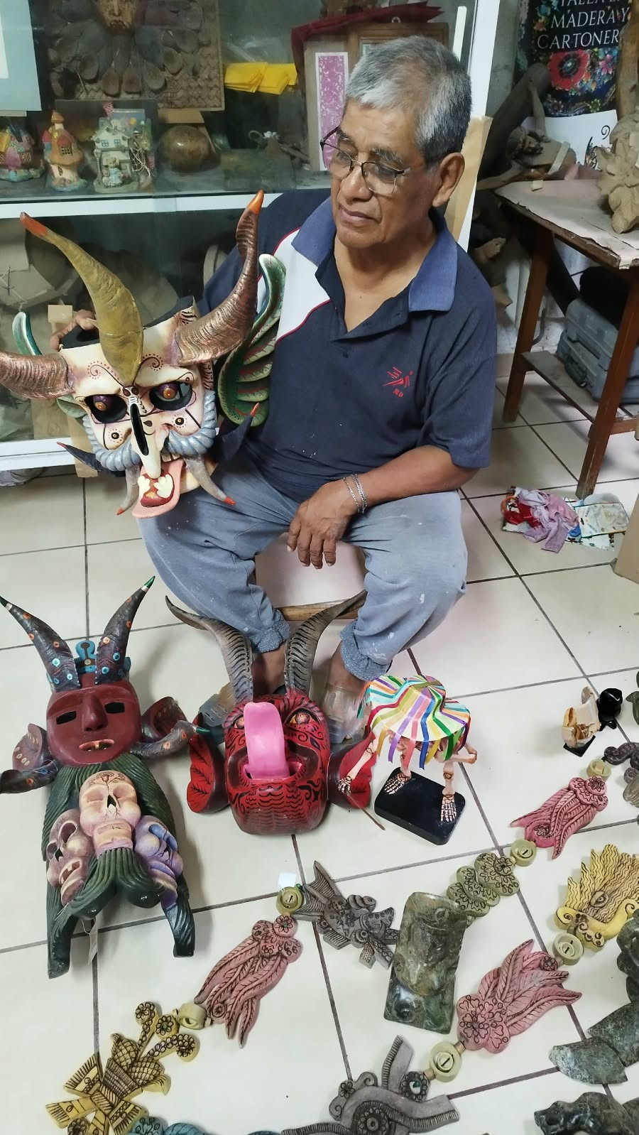 Persona sentada junto a máscaras y otras piezas artesanales